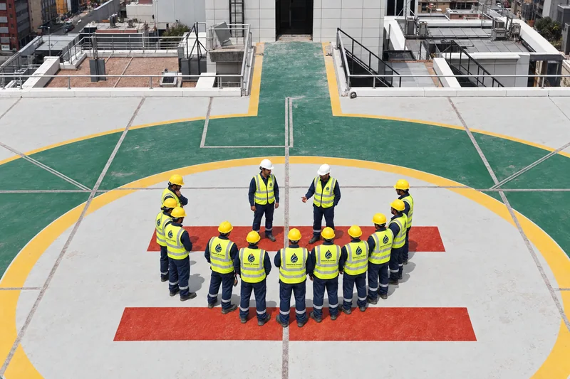People in high-visibility clothing and hard hats gathered in a semicircle on a marked rooftop.