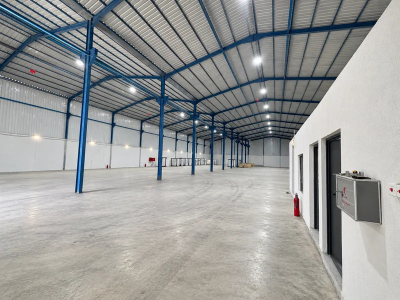 Warehouse interior with blue steel columns, a concrete floor and an enclosed office area.