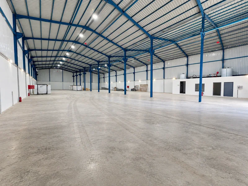 Wide warehouse interior with blue steel roof framing and a concrete floor.